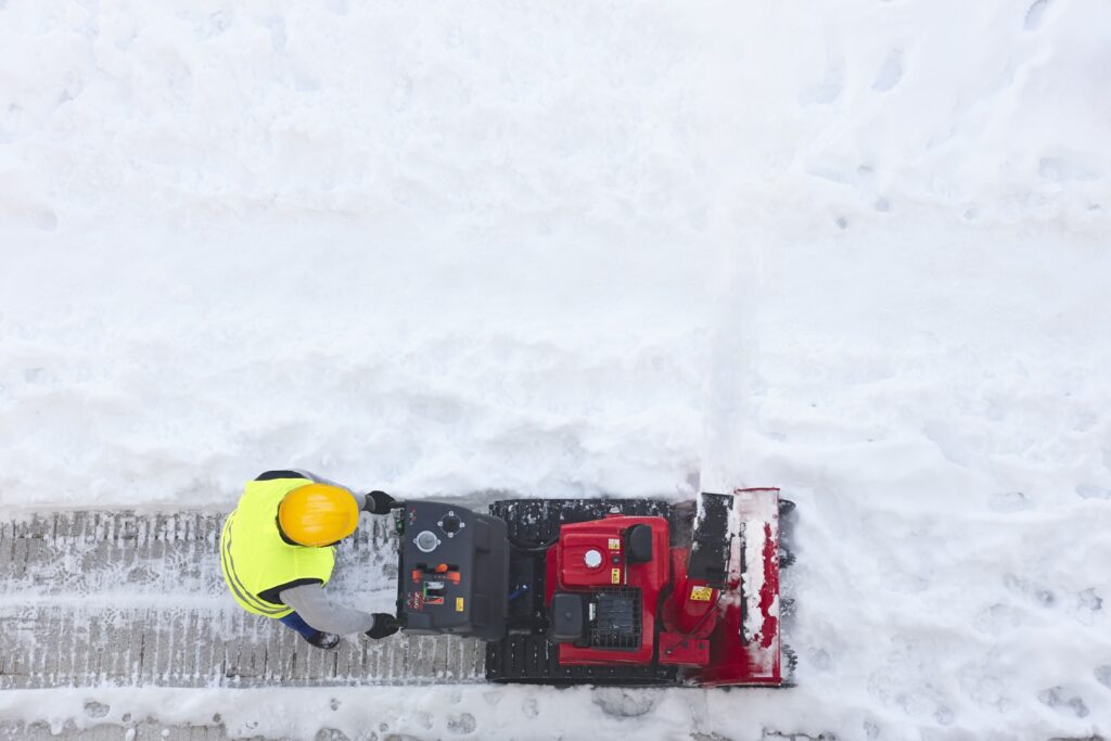 Worker cleaning snow on the sidewalk with a snowblower. Maintenance
