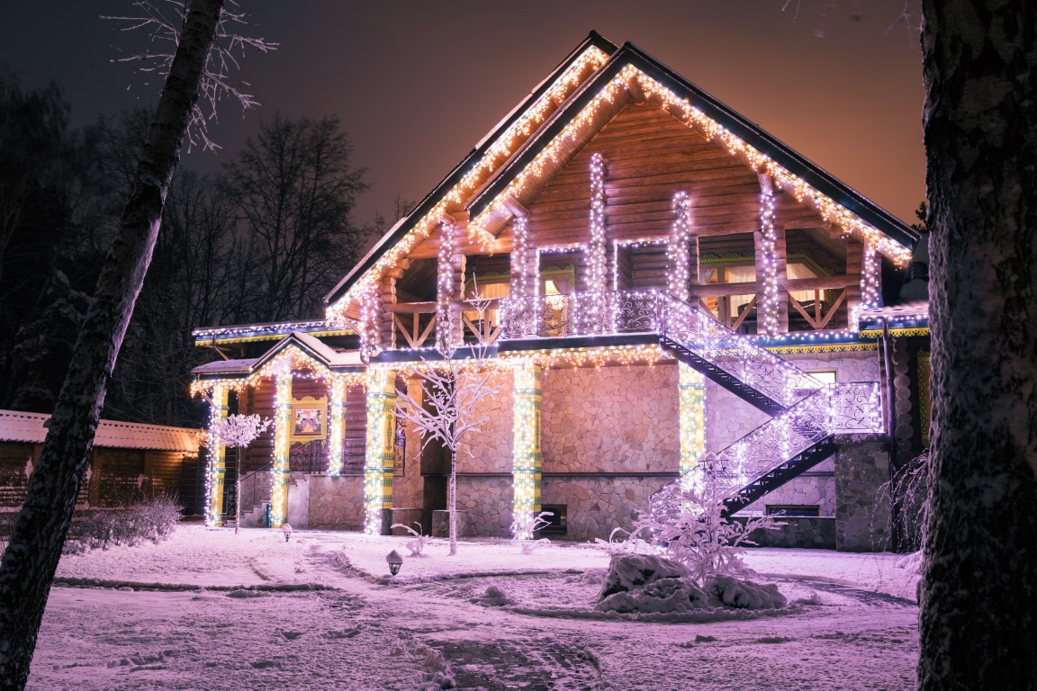 wooden house with lighting garlands in evening in forest